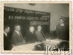 po 1945, Comodoro Rivadavia, Argentyna.
Inżynier Tadeusz Muszyński przemawia podczas uroczystości nadania członkowstwa honorowego prezesowi Związku Polaków w Argentynie Stanisławowi Pyzikowi. Za stołem siedzą F. Koprowski, prezes Buczek, Stanisław Pyzik, Szymański. Za jego plecami hasło: 