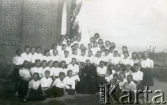 1943-1947, Kidugala, Tanganika.
Ojciec Justynian Maciaszek (1913-1959, proboszcz parafii w Kidugali, współtwórca ośrodka polskiego duszpasterstwa w argentyńskim Martin Coronado) z parafiankami.
Fot. ze zbiorów Archiwum Ojców Franciszkanów w Polskiej Misji Katolickiej w Martin Coronado w Argentynie, akta ojca Justyniana Maciaszka, reprodukcje cyfrowe w  Bibliotece Polskiej im. Ignacego Domeyki w Buenos Aires (Biblioteca Polaca Ignacio Domeyko) i w Ośrodku KARTA w Warszawie
