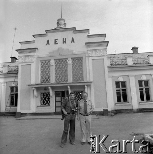 1977, Ust´-Kut, obwód irkucki, Rosyjska Federacyjna Socjalistyczna Republika Radziecka, ZSRR.
Budowa Bajkalsko-Amurskiej Magistrali Kolejowej. Operator i dziennikarz Mikołaj Nesterowicz (po lewej) oraz mężczyzna NN stoją przed budynkiem dworca kolejowego stacji 