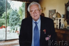 1999-2004, Londyn, Anglia, Wielka Brytania.
Janusz Cywiński w swoim mieszkaniu. Po prawej stronie marynarki widoczne odznaczenia, w tym Krzyż Oficerski Orderu Odrodzenia Polski.
Fot. NN, kolekcja Krystyny i Janusza Cywińskich, reprodukcje cyfrowe w Ośrodku KARTA