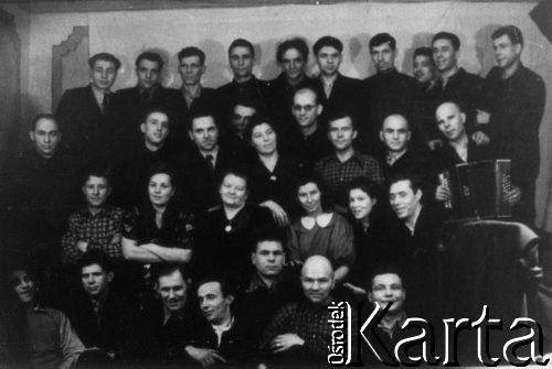 1955, Norylsk, Krasnojarski Kraj, ZSRR.
Polacy zwolnieni z sowieckich łagrów; dolny rząd od lewej: Edward Janczurewicz, Franciszek Czarkowski, Edward NN, NN, Kazimierz Szyłobryt, Stanisław Gotkowski, Bolesław Dubowicz; w drugim rzędzie siedzą od lewej: Misiura, Zuzanna Raubo, żona Edwarda NN (Rosjanka), Anna Górska, NN, NN; trzeci rząd od lewej: Zygmunt Czarnocki (stoi), Romuald Raubo (lub Marian Dowgiałło), Józef Wójcik, NN, Hanna Czarnocka, Kazimierz Pocześniak, Karol Gonet, Wiktor Wolski, NN (z harmonią); górny rząd pod ścianą od lewej: Jan Łukaszewicz, Stanisław Pszczółkowski, NN, NN, NN, Edward Jackiewicz, NN, Guzikowski (prawdopodobnie), NN.
Fot. NN, zbiory Ośrodka KARTA, udostępnił  Kazimierz Szyłobryt