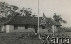 1944, Koja, Uganda.
Mężczyzna wciąga na maszt flagę brytyjską przed budynkiem administracji. W głębi budynek kancelarii i biur. [W osiedlu Koja w latach 1942-1948 mieszkało ok. 3000 Polaków, którzy z żołnierzami Armii Andersa zostali ewakuowani do Iranu].
Fot. NN, zbiory Ośrodka KARTA , udostępniła Maria Wierzchowska [AW - II/1681]