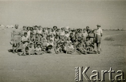 Marzec 1945, Karaczi, Indie.
Grupa dzieci i opiekunów w obozie dla polskich uchodźców. [Polscy uchodźcy w 1942 trafili do Iran.u wraz z nowoutworzonym Wojskiem Polskim pod dowództwem generała Władysława Andersa (w dwóch rzutach ewakuacyjnych z ZSRR w marcu i sierpniu). W sumie oprócz wojska dotarło tam 38 tysięcy Polaków, z czego ponad połowę stanowiły dzieci i młodzież. Około 10 tysięcy z nich trafiła potem do Indii, m.in. do dwóch obozów przejściowych w Karaczi]
Fot. NN, zbiory Ośrodka KARTA, kolekcja Adeli Duszy przekazała Halina Guść