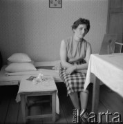 1950-1960, Nowa Huta, Kraków, Polska.
Surowe wnętrze jednego z pokoi w hotelu robotniczym. Na pierwszym planie kobieta siedząca na łóżku, obok na stoliku widoczna porcelanowa figurka  wilczura.
Fot. Irena Jarosińska, zbiory Ośrodka KARTA