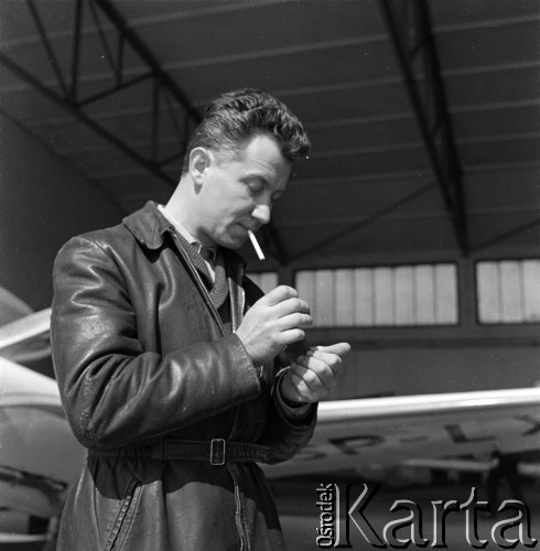 1960-1965, Katowice, woj. śląskie, Polska.
Pilot sanitarny w Zespole Lotnictwa Sanitarnego przy Wojskowej Stacji Pogotowia Ratunkowego Edward Makula (1930-1996) pali papierosa przed wejściem do hangaru, w którym stoi samolot Aero Ae-145.
Fot. Irena Jarosińska, zbiory Ośrodka KARTA
