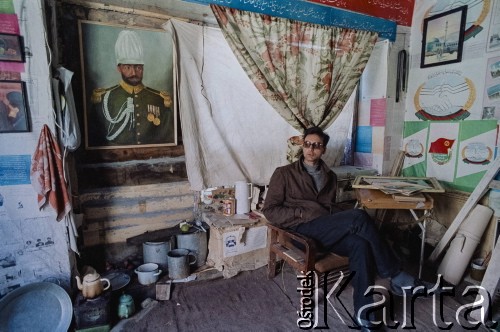 1992, Kabul, prowincja Kabul, Afganistan.
Mężczyzna w domu. Na ścianach pokoju wiszą plakaty i hasła o wymowie politycznej oraz portret afgańskiego władcy. Widoczny między innymi czerwony sztandar Ludowo-Demokratycznej Partii Afganistanu (LDPA) i godła Democratic Watan Party of Afganistan.
Fot. Irena Jarosińska, zbiory Ośrodka KARTA