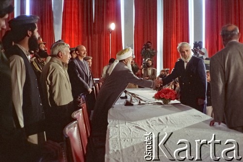 1992, Kabul, prowincja Kabul, Afganistan.
Konferencja prasowa afgańskiego polityka i przywódcy Sibghatullaha Modżaddediego (w białym turbanie). Od 28 kwietnia do 28 czerwca 1992 Modżaddedi pełnił funkcję tymczasowego prezydenta Afganistanu. Objął urząd po wycofaniu się wojsk radzieckich z Afganistanu, wkroczeniu  mudżahedinów do Kabulu i upadku wspieranych przez Sowietów komunistycznych rządów prezydenta Mohammada Nadżibullaha. Na zdjęciu Modżaddedi w rozmowie z Andrzejem Wawrzyniakiem, który w latach 1990-1993 pełnił urząd chargé d’affaires Rzeczpospolitej Polskiej w Afganistanie.
Fot. Irena Jarosińska, zbiory Ośrodka KARTA