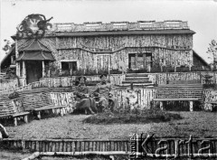 1914-1915, Rosja.
Dwaj żołnierze siedzą przed budynkiem z drewna brzozowego. Nad wejściem do budynku wycięte z drewna godło - orzeł biały. 
Zdjęcie pochodzi z albumu Zdzisława Poklewskiego-Koziełł.
Fot. Zdzisław Poklewski-Koziełł, zbiory Ośrodka KARTA, przekazała Hanna Kunachowicz