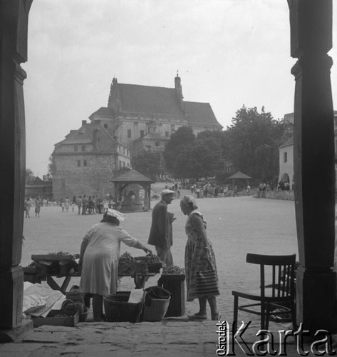 Lipiec 1956, Kazimierz Dolny, Polska.
Kazimierski Rynek, kobieta sprzedające owoce. W tle zabytkowa studnia i kościół farny. 
Fot. Romuald Broniarek, zbiory Ośrodka KARTA