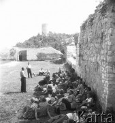 Lipiec 1956, Kazimierz Dolny, Polska.
Grupa turystów odpoczywa w cieniu muru na dziedzińcu zamku Kazimierza Wielkiego. W tle wieża zbudowana w czasach Władysława Łokietka.
Fot. Romuald Broniarek, zbiory Ośrodka KARTA