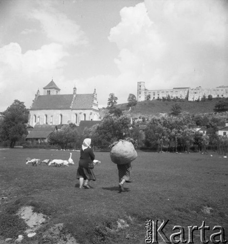 Lipiec 1957, Janowiec, Polska.
Dwie wiejskie kobiety i stadko gęsi, w tle kościół parafialny św. Stanisława i św. Małgorzaty i ruiny renesansowego zamku wybudowanego w XVI w. przez Mikołaja Firleja.
Fot. Romuald Broniarek, zbiory Ośrodka KARTA