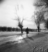 Styczeń 1958, woj. Białystok, Polska.
Kobieta idąca zaśnieżoną drogą, na horyzoncie zabudowania wsi.
Fot. Romuald Broniarek, zbiory Ośrodka KARTA