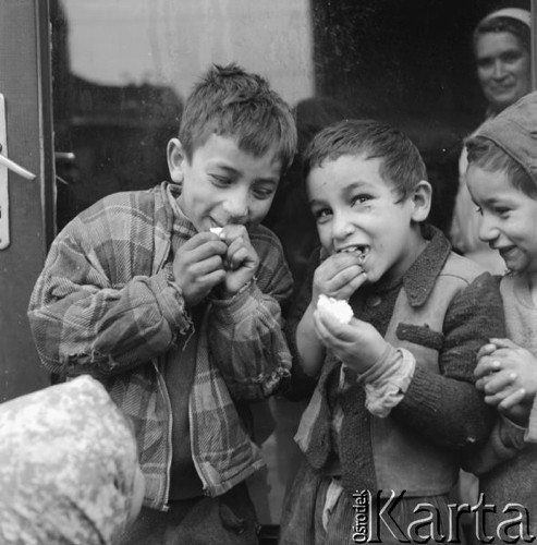 Kwiecień 1958, Warszawa, Polska. 
Cygańskie dzieci jedzą bułkę przed kuchnią stołówki. Za zamkniętymi drzwiami stoi kobieta w fartuchu.
Fot. Romuald Broniarek, zbiory Ośrodka KARTA