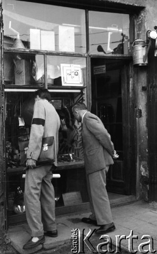 Wrzesień 1958, Warszawa, Polska.
Mężczyźni oglądają towary w witrynie sklepu z artykułami żelaznymi. Jeden z mężczyzn ma na rękawie marynarki żałobną opaskę. Nad drzwiami sklepu wisi blaszana konewka.
Fot. Romuald Broniarek, zbiory Ośrodka KARTA