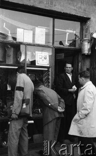 Wrzesień 1958, Warszawa, Polska.
Mężczyźni oglądają towary w witrynie sklepu z artykułami żelaznymi. Jeden z mężczyzn ma na rękawie marynarki żałobną opaskę. Nad drzwiami sklepu wisi blaszana konewka.
Fot. Romuald Broniarek, zbiory Ośrodka KARTA