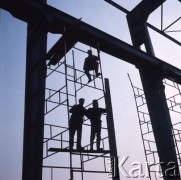 Marzec 1975, Dąbrowa Górnicza, woj. Katowice, Polska.
Budowa Huty Katowice, wznoszenie stalowej konstrukcji hali produkcyjnej, robotnicy w kaskach ochronnych na rusztowaniu.
Fot. Romuald Broniarek/KARTA
