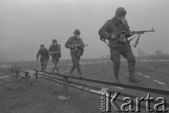 Luty 1976, Polska.
Słuchacze Wyższej Oficerskiej Szkoły Wojsk Zmechanizowanych we Wrocławiu podczas ćwiczeń na poligonie. Żołnierze w maskach przeciwgazowych i z karabinami przechodzą po równoważni.
Fot. Romuald Broniarek/KARTA