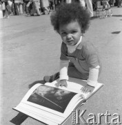 Maj 1976, Warszawa, Polska.
Kiermasz Książki przed Pałacem Kultury i Nauki, czarnoskóre dziecko oglądające album o sztuce.
Fot. Romuald Broniarek/KARTA