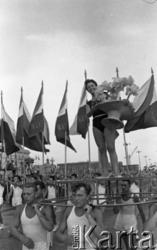 22.07.1959, Warszawa, Polska.
Uroczyste obchody piętnastolecia PRL z udziałem Nikity Chruszczowa, I sekretarza KC KPZR. Młodzież z flagami podczas defilady. Na pierwszym planie młodzi mężczyźni niosą platformę, na której stoi kobieta z koszem kwiatów.
Fot. Romuald Broniarek/KARTA