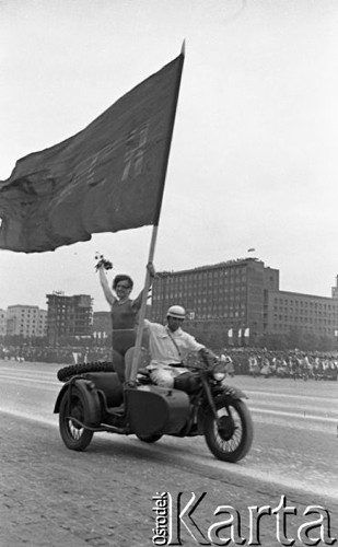 22.07.1959, Warszawa, Polska.
Uroczyste obchody piętnastolecia PRL z udziałem Nikity Chruszczowa, I sekretarza KC KPZR. Kobieta ze sztandarem stoi w koszu motocykla.
Fot. Romuald Broniarek/KARTA