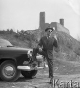 Maj 1960, Chęciny k/Kielc, Polska.
Mężczyzna w garniturze i kapeluszu opiera się o zderzak samochodu, w tle ruiny zamku Władysława Łokietka i Kazimierza Wielkiego.
Fot. Romuald Broniarek/KARTA