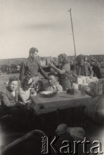 Czerwiec 1946, Kuźnica Białostocka, Polska.
Siedemnasty i ostatni transport repatriantów z Gudogaj do Łuczan. Postój na stacji w Kuźnicy. Za stołem siedzi pełnomocniczka transportu ze strony polskiej Aldona Jackiewicz, obok niej pełnomocnik rosyjski Agapow. W tle pociąg towarowy, którym jechali repatrianci.
Fot. NN, zbiory Ośrodka KARTA, udostępniła Aldona Nikoniuk.

