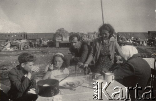 Czerwiec 1946, Kuźnica Białostocka, Polska.
Siedemnasty i ostatni transport repatriantów z Gudogaj do Łuczan. Posiłek na stacji w Kuźnicy, za stołem siedzi polska pełnomocniczka transportu Aldona Jackiewicz. W tle pociąg, którym jechali repatrianci.
Fot. NN, zbiory Ośrodka KARTA, udostępniła Aldona Nikoniuk.

