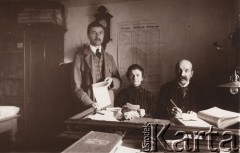 1916, Lwów
 Pracownicy urzędu - komisja przyjmująca od osób fizycznych Podatki na cele wojskowe, na stole leży księga z tytułem: 