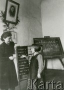 Jesień 1939, Polska.
Nauczycielka i uczennica przy liczydłach, w tle tablica, na której wypisano polski alfabet.
Fot. NN, zbiory Ośrodka KARTA, udostępnił Krzysztof Jasiewicz [sygn. oryginalna 0-18735]
 
