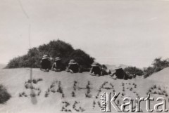 Kwiecień 1942, Sahara.
Samodzielna Brygada Strzelców Karpackich - żołnierze odpoczywają na pustynnym piasku. Na pierwszym planie widoczny jest również - utworzony z kęp trawy - napis: 