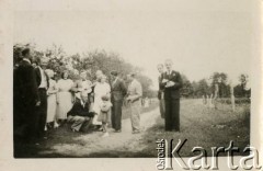 Lata 40., brak miejsca.
Grupa odświętnie ubranych osób stojących przy wiejskiej drodze. Na dalszym planie widoczny sad oraz pole uprawne.
Fot. NN, kolekcja Eugeniusza Lewickiego, zbiory Ośrodka KARTA