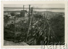 1929-1939, okolice Brześcia nad Bugiem, woj. poleskie, Rzeczpospolita Polska.
Robotnicy podczas pracy na terenie budowy. Widoczny między innymi kefar parowy - urządzenie służące do wbijania pali w ziemne podłoże.
Kanał Muchawiecki (Kanał Dniepr-Bug, zwany również Kanałem Królewskim lub Kanałem Rzeczypospolitej) otwarty w 1848 roku kanał żeglowny łączący Dniepr z Wisłą poprzez Pinę (dopływ Prypeci) i Muchawiec (prawostronny dopływ Bugu) stanowiący część szlaku wodnego łączącego Morze Bałtyckie z Morzem Czarnym. Pierwszy odcinek Kanału zbudowano w latach 1775-1784, następnie, w latach 1846-1848, Kanał był rozbudowywany przez władze rosyjskie. W latach 1929-1939, w czasach administracji II Rzeczypospolitej, poddawany gruntowym pracom remontowym. 
Fot. NN, kolekcja Eugeniusza Lewickiego, zbiory Ośrodka KARTA