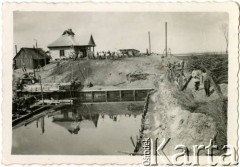 1929-1939, okolice Brześcia nad Bugiem, woj. poleskie, Rzeczpospolita Polska.
Pracownicy na terenie budowy podczas pracy przy zbiorniku z wodą.
Kanał Muchawiecki (Kanał Dniepr-Bug, zwany również Kanałem Królewskim lub Kanałem Rzeczypospolitej) otwarty w 1848 roku kanał żeglowny łączący Dniepr z Wisłą poprzez Pinę (dopływ Prypeci) i Muchawiec (prawostronny dopływ Bugu) stanowiący część szlaku wodnego łączącego Morze Bałtyckie z Morzem Czarnym. Pierwszy odcinek Kanału zbudowano w latach 1775-1784, następnie, w latach 1846-1848, Kanał był rozbudowywany przez władze rosyjskie. W latach 1929-1939, w czasach administracji II Rzeczypospolitej, poddawany gruntowym pracom remontowym. 
Fot. NN, kolekcja Eugeniusza Lewickiego, zbiory Ośrodka KARTA