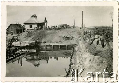 1929-1939, okolice Brześcia nad Bugiem, woj. poleskie, Rzeczpospolita Polska.
Pracownicy na terenie budowy podczas pracy przy zbiorniku z wodą.
Kanał Muchawiecki (Kanał Dniepr-Bug, zwany również Kanałem Królewskim lub Kanałem Rzeczypospolitej) otwarty w 1848 roku kanał żeglowny łączący Dniepr z Wisłą poprzez Pinę (dopływ Prypeci) i Muchawiec (prawostronny dopływ Bugu) stanowiący część szlaku wodnego łączącego Morze Bałtyckie z Morzem Czarnym. Pierwszy odcinek Kanału zbudowano w latach 1775-1784, następnie, w latach 1846-1848, Kanał był rozbudowywany przez władze rosyjskie. W latach 1929-1939, w czasach administracji II Rzeczypospolitej, poddawany gruntowym pracom remontowym. 
Fot. NN, kolekcja Eugeniusza Lewickiego, zbiory Ośrodka KARTA