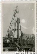 1929-1939, okolice Brześcia nad Bugiem, woj. poleskie, Rzeczpospolita Polska.
Robotnicy podczas pracy na terenie budowy obsługują kefar parowy - urządzenie służące do wbijania pali w ziemne podłoże.
Kanał Muchawiecki (Kanał Dniepr-Bug, zwany również Kanałem Królewskim lub Kanałem Rzeczypospolitej) otwarty w 1848 roku kanał żeglowny łączący Dniepr z Wisłą poprzez Pinę (dopływ Prypeci) i Muchawiec (prawostronny dopływ Bugu) stanowiący część szlaku wodnego łączącego Morze Bałtyckie z Morzem Czarnym. Pierwszy odcinek Kanału zbudowano w latach 1775-1784, następnie, w latach 1846-1848, Kanał był rozbudowywany przez władze rosyjskie. W latach 1929-1939, w czasach administracji II Rzeczypospolitej, poddawany gruntowym pracom remontowym. 
Fot. NN, kolekcja Eugeniusza Lewickiego, zbiory Ośrodka KARTA