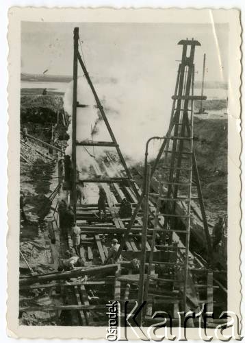 1929-1939, okolice Brześcia nad Bugiem, woj. poleskie, Rzeczpospolita Polska.
Teren budowy. Robotnicy obsługują kefar parowy - urządzenie służące do wbijania pali w ziemne podłoże.
Kanał Muchawiecki (Kanał Dniepr-Bug, zwany również Kanałem Królewskim lub Kanałem Rzeczypospolitej) otwarty w 1848 roku kanał żeglowny łączący Dniepr z Wisłą poprzez Pinę (dopływ Prypeci) i Muchawiec (prawostronny dopływ Bugu) stanowiący część szlaku wodnego łączącego Morze Bałtyckie z Morzem Czarnym. Pierwszy odcinek Kanału zbudowano w latach 1775-1784, następnie, w latach 1846-1848, Kanał był rozbudowywany przez władze rosyjskie. W latach 1929-1939, w czasach administracji II Rzeczypospolitej, poddawany gruntowym pracom remontowym. 
Fot. NN, kolekcja Eugeniusza Lewickiego, zbiory Ośrodka KARTA