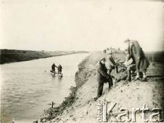 1929-1939, okolice Brześcia nad Bugiem, woj. poleskie, Rzeczpospolita Polska.
Grupa mężczyzn stoi na wale na brzegu rzeki. 1. z prawej widoczny Eugeniusz Lewicki.
Kanał Muchawiecki (Kanał Dniepr-Bug, zwany również Kanałem Królewskim lub Kanałem Rzeczypospolitej) otwarty w 1848 roku kanał żeglowny łączący Dniepr z Wisłą poprzez Pinę (dopływ Prypeci) i Muchawiec (prawostronny dopływ Bugu) stanowiący część szlaku wodnego łączącego Morze Bałtyckie z Morzem Czarnym. Pierwszy odcinek Kanału zbudowano w latach 1775-1784, następnie, w latach 1846-1848, Kanał był rozbudowywany przez władze rosyjskie. W latach 1929-1939, w czasach administracji II Rzeczypospolitej, poddawany gruntowym pracom remontowym. 
Fot. NN, kolekcja Eugeniusza Lewickiego, zbiory Ośrodka KARTA