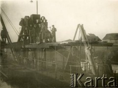 1929-1939, okolice Brześcia nad Bugiem, woj. poleskie, Rzeczpospolita Polska.
Pogłębiarka podczas pracy. Na pokładzie jednostki, pośród mężczyzn, widoczny Eugeniusz Lewicki (w berecie i płaszczu, 3. z prawej). Obok niego, w kożuchu oraz czapce, urzędnik państwowy nadzorujący przebieg prac.
Kanał Muchawiecki (Kanał Dniepr-Bug, zwany również Kanałem Królewskim lub Kanałem Rzeczypospolitej) otwarty w 1848 roku kanał żeglowny łączący Dniepr z Wisłą poprzez Pinę (dopływ Prypeci) i Muchawiec (prawostronny dopływ Bugu) stanowiący część szlaku wodnego łączącego Morze Bałtyckie z Morzem Czarnym. Pierwszy odcinek Kanału zbudowano w latach 1775-1784, następnie, w latach 1846-1848, Kanał był rozbudowywany przez władze rosyjskie. W latach 1929-1939, w czasach administracji II Rzeczypospolitej, poddawany gruntowym pracom remontowym. 
Fot. NN, kolekcja Eugeniusza Lewickiego, zbiory Ośrodka KARTA