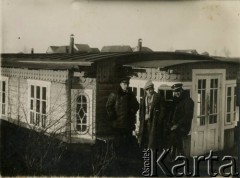 Około 1936, prawdopodobnie Sieliszcze, woj. poleskie, Rzeczpospolita Polska.
Grupa mężczyzn stoi przed drewnianym parterowym budynkiem. W środku stoi Eugeniusz Lewicki, obok niego w kożuchu i czapce urzędnik państwowy.
Kanał Muchawiecki (Kanał Dniepr-Bug, zwany również Kanałem Królewskim lub Kanałem Rzeczypospolitej) otwarty w 1848 roku kanał żeglowny łączący Dniepr z Wisłą poprzez Pinę (dopływ Prypeci) i Muchawiec (prawostronny dopływ Bugu) stanowiący część szlaku wodnego łączącego Morze Bałtyckie z Morzem Czarnym. Pierwszy odcinek Kanału zbudowano w latach 1775-1784, następnie, w latach 1846-1848, Kanał był rozbudowywany przez władze rosyjskie. W latach 1929-1939, w czasach administracji II Rzeczypospolitej, poddawany gruntowym pracom remontowym. 
Fot. NN, zbiory Ośrodka KARTA
