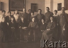 30.12.1919, Wilno, Polska.
 Grupa osób - kobiety w cywilnych ubraniach i polscy oficerowie. Oficer stojący pierwszy od prawej ma przy pasie szablę wz. 1917; kobieta stojąca za nim ma przypięty do bluzki okrągły znaczek Polskiego Czerwonego Krzyża; dwaj kolejni oficerowie na prawej kieszeni munduru mają przypięte odznaki „Wielkanoc w Wilnie”. Czwarty od lewej stoi dr Eugeniusz Budzyński (z bagnetem przy pasie). Druga kobieta siedząca od prawej ma przypiętą do bluzki odznakę sióstr  miłosierdzia PCK, oficer siedzący w środku ma w klapie munduru odznakę „Wielkanoc w Wilnie”.  
 Fot. Jan Bułhak, zbiory Ośrodka KARTA, udostępnił Stanisław Blichiewicz
   
