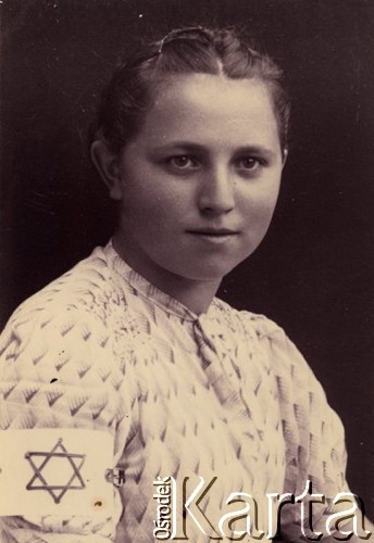 1939-1941, Kozienice, Polska.
Portret młodej Żydówki z opaską na rękawie.
Zdjęcie wykonane w atelier fotograficznym żydowskiego fotografa Chaima Bernemana. Przed wojną zakład mieścił się w Kozienicach na rogu ulic Warszawskiej i Maciejowickiej, przed wybuchem wojny albo już w czasie niemieckiej okupacji  został przeniesiony na ulicę Lubelską 13. Cała kolekcja jest datowana na okres od drugiej połowy lat 30-tych do roku 1941, kiedy Chaim Berneman wraz z rodziną został zesłany do obozu pracy w Wolanowie. Berneman zmarł po ucieczce z obozu.
Fot. Chaim Berneman (Chaim Berman), zbiory Ośrodka KARTA