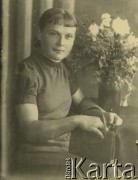 Druga połowa lat 30. do 1941, Kozienice, Polska.
Portret młodej kobiety z torebką, na stoliku stoi wazon z kwiatami.
Zdjęcie wykonane w atelier fotograficznym żydowskiego fotografa Chaima Bernemana. Przed wojną zakład mieścił się w Kozienicach na rogu ulic Warszawskiej i Maciejowickiej, przed wybuchem wojny albo już w czasie niemieckiej okupacji  został przeniesiony na ulicę Lubelską 13. Cała kolekcja jest datowana na okres od drugiej połowy lat 30-tych do roku 1941, kiedy Chaim Berneman wraz z rodziną został zesłany do obozu pracy w Wolanowie. Berneman zmarł po ucieczce z obozu.
Fot. Chaim Berneman (Chaim Berman), zbiory Ośrodka KARTA