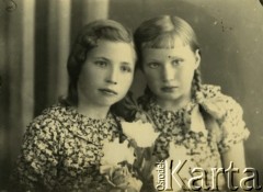 Druga połowa lat 30. do 1941, Kozienice, Polska.
Portret dwóch dziewczynek we wzorzystych sukienkach z bukietem kwiatów.
Zdjęcie wykonane w atelier fotograficznym żydowskiego fotografa Chaima Bernemana. Przed wojną zakład mieścił się w Kozienicach na rogu ulic Warszawskiej i Maciejowickiej, przed wybuchem wojny albo już w czasie niemieckiej okupacji  został przeniesiony na ulicę Lubelską 13. Cała kolekcja jest datowana na okres od drugiej połowy lat 30-tych do roku 1941, kiedy Chaim Berneman wraz z rodziną został zesłany do obozu pracy w Wolanowie. Berneman zmarł po ucieczce z obozu.
Fot. Chaim Berneman (Chaim Berman), zbiory Ośrodka KARTA