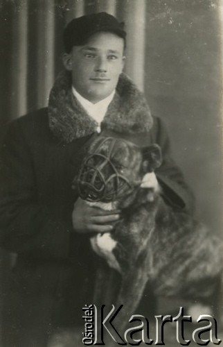 Druga połowa lat 30. do 1941, Kozienice, Polska.
Portret chłopaka z psem w kagańcu.
Zdjęcie wykonane w atelier fotograficznym żydowskiego fotografa Chaima Bernemana. Przed wojną zakład mieścił się w Kozienicach na rogu ulic Warszawskiej i Maciejowickiej, przed wybuchem wojny albo już w czasie niemieckiej okupacji  został przeniesiony na ulicę Lubelską 13. Cała kolekcja jest datowana na okres od drugiej połowy lat 30-tych do roku 1941, kiedy Chaim Berneman wraz z rodziną został zesłany do obozu pracy w Wolanowie. Berneman zmarł po ucieczce z obozu.
Fot. Chaim Berneman (Chaim Berman), zbiory Ośrodka KARTA