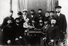 Druga połowa lat 30. do 1941, Kozienice, Polska.
Grupa Żydów przy stole.
Zdjęcie wykonane w atelier fotograficznym żydowskiego fotografa Chaima Bernemana. Przed wojną zakład mieścił się w Kozienicach na rogu ulic Warszawskiej i Maciejowickiej, przed wybuchem wojny albo już w czasie niemieckiej okupacji  został przeniesiony na ulicę Lubelską 13. Cała kolekcja jest datowana na okres od drugiej połowy lat 30-tych do roku 1941, kiedy Chaim Berneman wraz z rodziną został zesłany do obozu pracy w Wolanowie. Berneman zmarł po ucieczce z obozu.
Fot. Chaim Berneman (Chaim Berman), zbiory Ośrodka KARTA