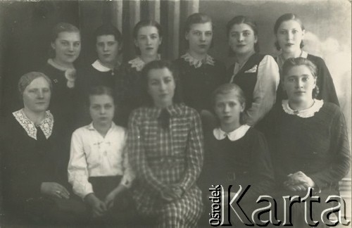 Druga połowa lat 30. do 1939, Kozienice, Polska.
Uczennice gimnazjum i nauczycielki.
Zdjęcie wykonane w atelier fotograficznym żydowskiego fotografa Chaima Bernemana. Przed wojną zakład mieścił się w Kozienicach na rogu ulic Warszawskiej i Maciejowickiej, przed wybuchem wojny albo już w czasie niemieckiej okupacji został przeniesiony na ulicę Lubelską 13. Cała kolekcja jest datowana na okres od drugiej połowy lat 30-tych do roku 1941, kiedy Chaim Berneman wraz z rodziną został zesłany do obozu pracy w Wolanowie. Berneman zmarł po ucieczce z obozu.
Fot. Chaim Berneman (Chaim Berman), zbiory Ośrodka KARTA