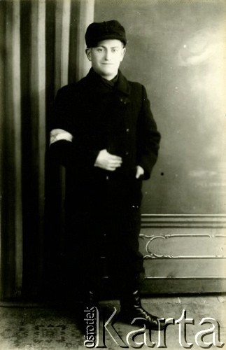 1939-1941, Kozienice, Polska.
Portret młodego mężczyzny z opaską na rękawie płaszcza.
Zdjęcie wykonane w atelier fotograficznym żydowskiego fotografa Chaima Bernemana. Przed wojną zakład mieścił się w Kozienicach na rogu ulic Warszawskiej i Maciejowickiej, przed wybuchem wojny albo już w czasie niemieckiej okupacji  został przeniesiony na ulicę Lubelską 13. Cała kolekcja jest datowana na okres od drugiej połowy lat 30-tych do roku 1941, kiedy Chaim Berneman wraz z rodziną został zesłany do obozu pracy w Wolanowie. Berneman zmarł po ucieczce z obozu.
Fot. Chaim Berneman (Chaim Berman), zbiory Ośrodka KARTA