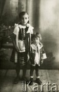 Druga połowa lat 30. do 1941, Kozienice, Polska.
Portret dwójki dzieci w strojach ludowych.
Zdjęcie wykonane w atelier fotograficznym żydowskiego fotografa Chaima Bernemana. Przed wojną zakład mieścił się w Kozienicach na rogu ulic Warszawskiej i Maciejowickiej, przed wybuchem wojny albo już w czasie niemieckiej okupacji został przeniesiony na ulicę Lubelską 13. Cała kolekcja jest datowana na okres od drugiej połowy lat 30-tych do roku 1941, kiedy Chaim Berneman wraz z rodziną został zesłany do obozu pracy w Wolanowie. Berneman zmarł po ucieczce z obozu.
Fot. Chaim Berneman (Chaim Berman), zbiory Ośrodka KARTA