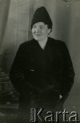 Druga połowa lat 30. do 1941, Kozienice, Polska.
Portret kobiety w futerku z mufką i w barankowej czapce.
Zdjęcie wykonane w atelier fotograficznym żydowskiego fotografa Chaima Bernemana. Przed wojną zakład mieścił się w Kozienicach na rogu ulic Warszawskiej i Maciejowickiej, przed wybuchem wojny albo już w czasie niemieckiej okupacji został przeniesiony na ulicę Lubelską 13. Cała kolekcja jest datowana na okres od drugiej połowy lat 30-tych do roku 1941, kiedy Chaim Berneman wraz z rodziną został zesłany do obozu pracy w Wolanowie. Berneman zmarł po ucieczce z obozu.
Fot. Chaim Berneman (Chaim Berman), zbiory Ośrodka KARTA