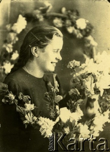 Druga połowa lat 30. do 1941, Kozienice, Polska.
Portret dziewczyny w girlandzie kwiatów.
Zdjęcie wykonane w atelier fotograficznym żydowskiego fotografa Chaima Bernemana. Przed wojną zakład mieścił się w Kozienicach na rogu ulic Warszawskiej i Maciejowickiej, przed wybuchem wojny albo już w czasie niemieckiej okupacji został przeniesiony na ulicę Lubelską 13. Cała kolekcja jest datowana na okres od drugiej połowy lat 30-tych do roku 1941, kiedy Chaim Berneman wraz z rodziną został zesłany do obozu pracy w Wolanowie. Berneman zmarł po ucieczce z obozu.
Fot. Chaim Berneman (Chaim Berman), zbiory Ośrodka KARTA